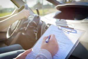 A driving instructor takes notes as a student drives.