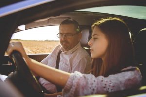 A driving student behind the wheel, with an instructor sitting beside her.