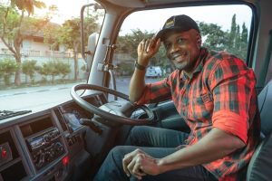A man smiles as he sits behind the wheel in the cab of a tractor-trailer.