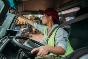 Trucker wearing reflective vest sitting in driver’s seat and adjusting mirror
